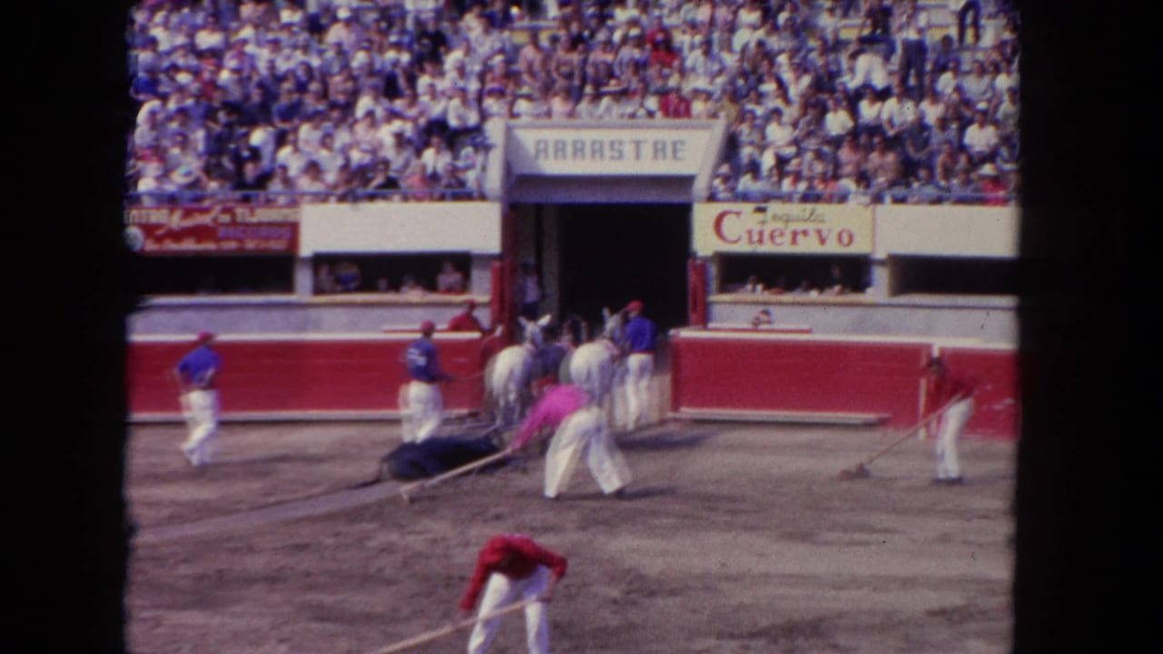 Wide bullring view showing arena workers near the ARRASTRE gate, horses, and packed stands at a 1962 Los Angeles corrida captured on 8mm film.