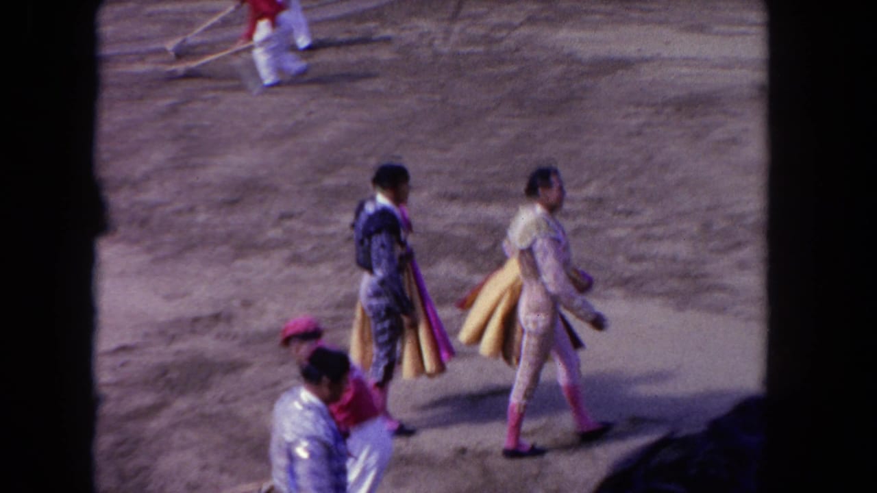 Three matadors in colorful silk and lamé costumes walk across a sandy bullfighting arena, shot from an elevated spectator position.