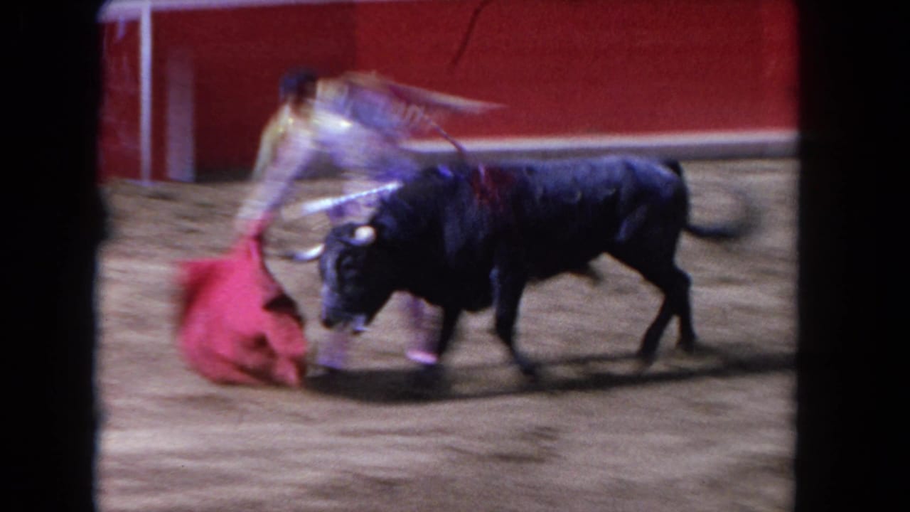 Bull charging toward a matador swinging a red cape in a sand arena, 8mm color, with action blur.