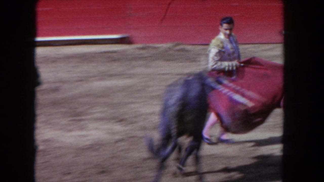 Matador in ornate jacket sweeps red cape as dark bull charges past, 8mm film frame.