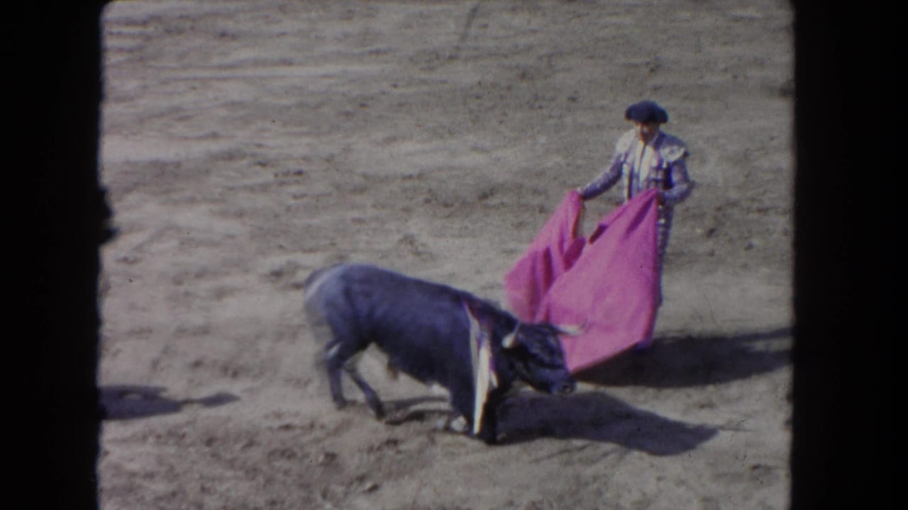 Matador sweeps pink cape as bull passes close in dusty arena, shot from elevated spectator position