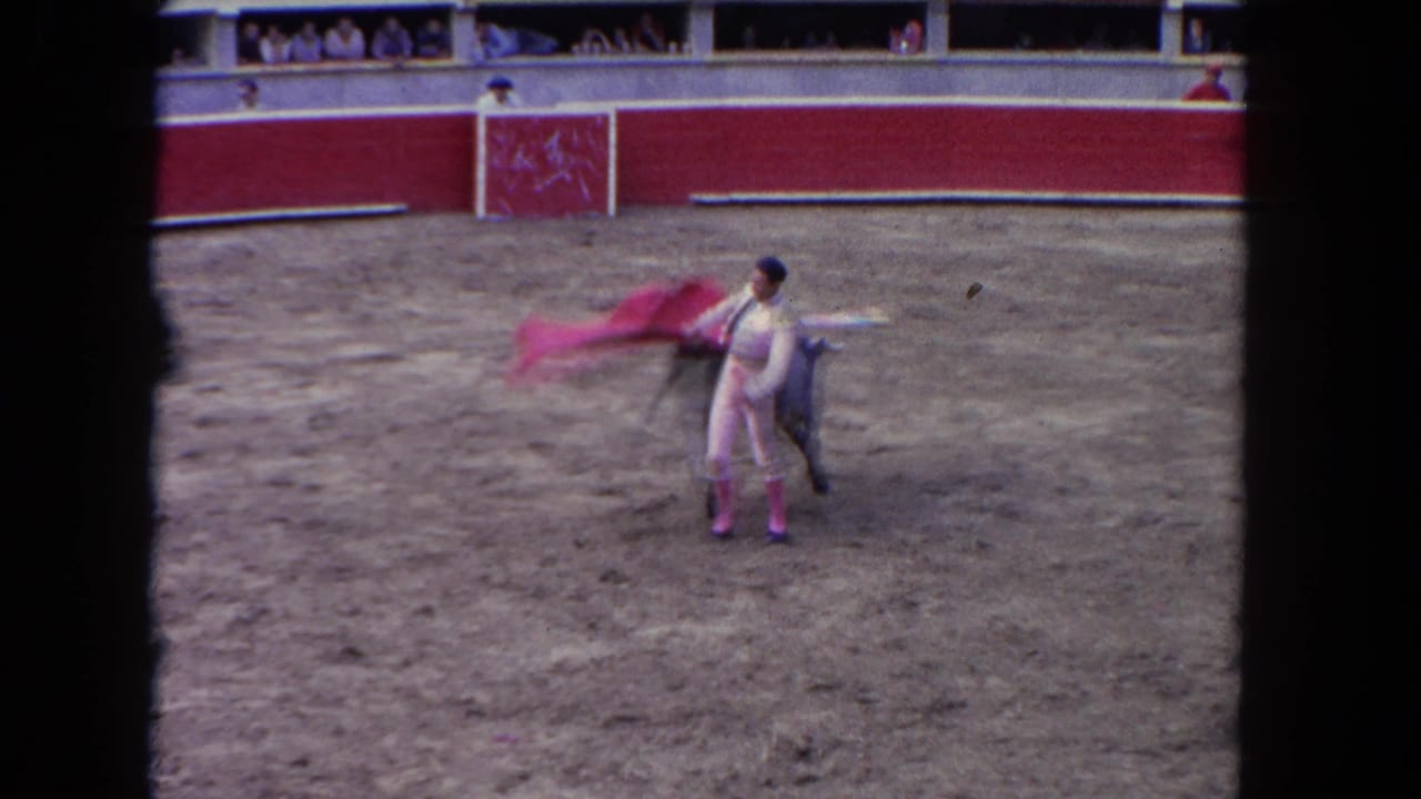 1962 8mm: matador extends cape after a pass with bull at left; crowd visible in distant tiered arena stands