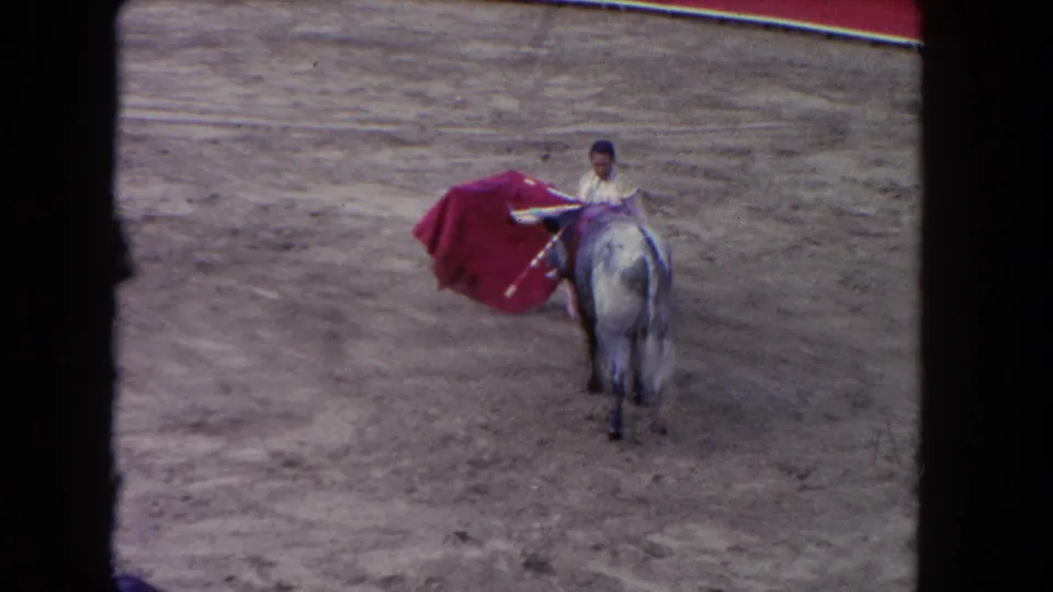1962 8mm home movie: bullfighter with outstretched red muleta cape in Los Angeles arena; pale horse at right may indicate a picador is present.