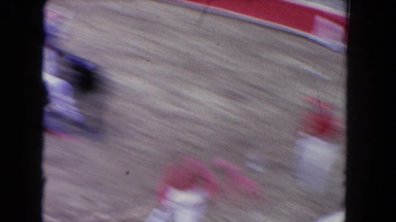 Heavy motion blur captures fast arena action, blurred figures in pink and white tones against sandy floor.