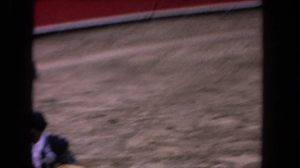 Near-empty arena floor between action sequences, partial figures at lower frame edge; 8mm home-movie footage circa 1962.