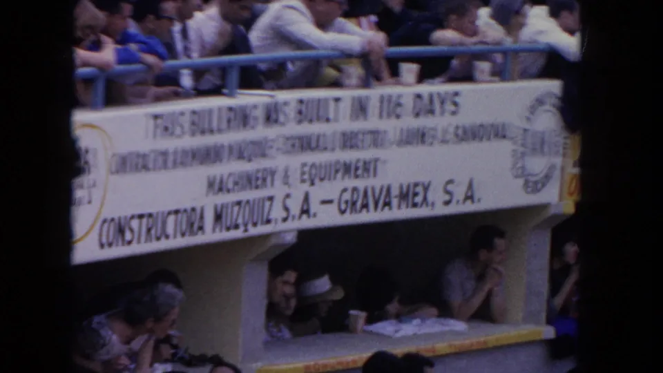 Close-up of a bilingual construction sign inside a 1962 bullring crediting Mexican firms Constructora Muzquiz S.A. and Grava-Mex S.A.; spectators in period dress seated below the sign.