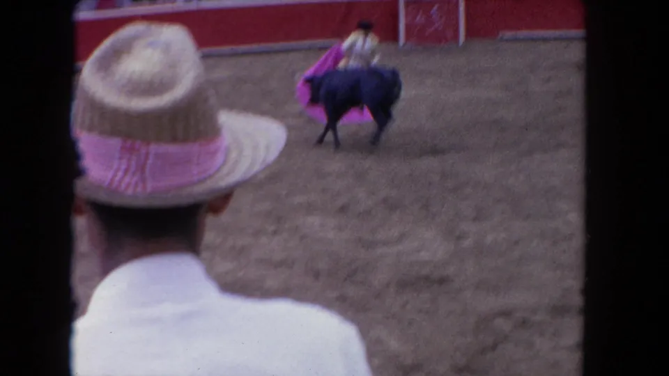 1960s 8mm home movie: spectator in straw hat with pink band watches matador and charging bull in an arena, possibly Los Angeles, ca. 1962.