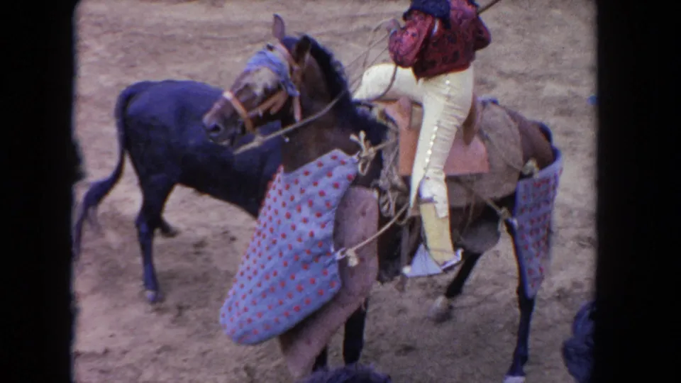 8mm close-up of a padded arena horse and mounted rider in a red patterned jacket and pale trousers, from a 1962 Los Angeles corrida-style performance.