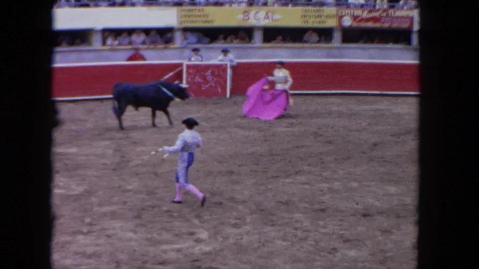1962 color 8mm wide arena shot showing matadors, a dark bull, advertising banners on the red barrera, and packed spectator stands.