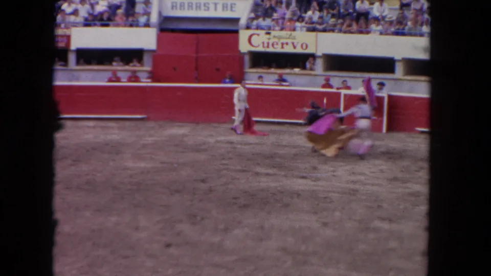 1960s corrida mid-action: matador maneuvering with magenta capote near red barrera, Tequila Cuervo and ARRASTRE signs visible above packed bleachers.