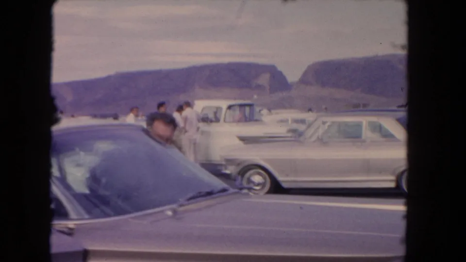 A man in a light shirt peeks over the roofline of a classic car in this 1962 Los Angeles home-movie frame.