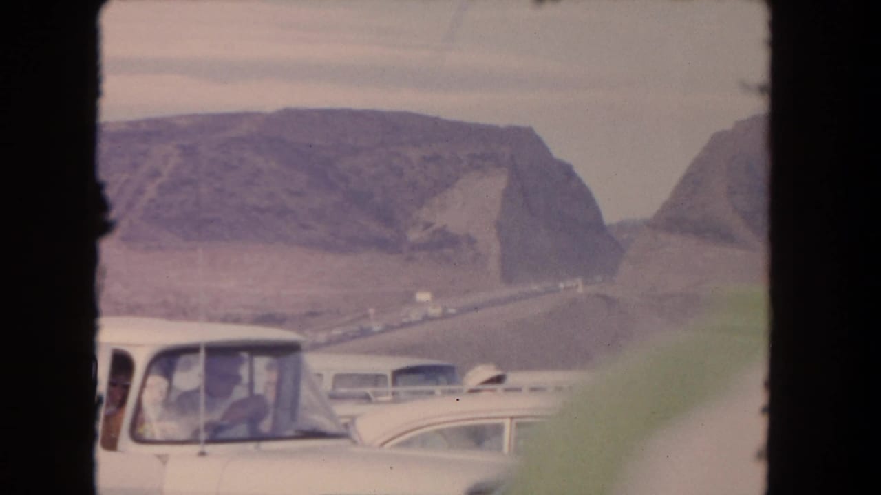 Classic cars in traffic with dry mountains behind them.