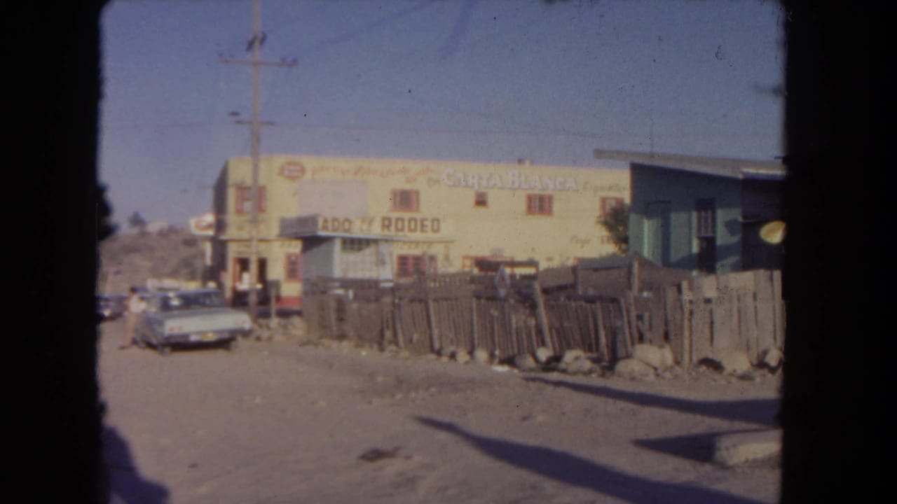 Signed yellow building beside a fence and parked car, with utility lines above.