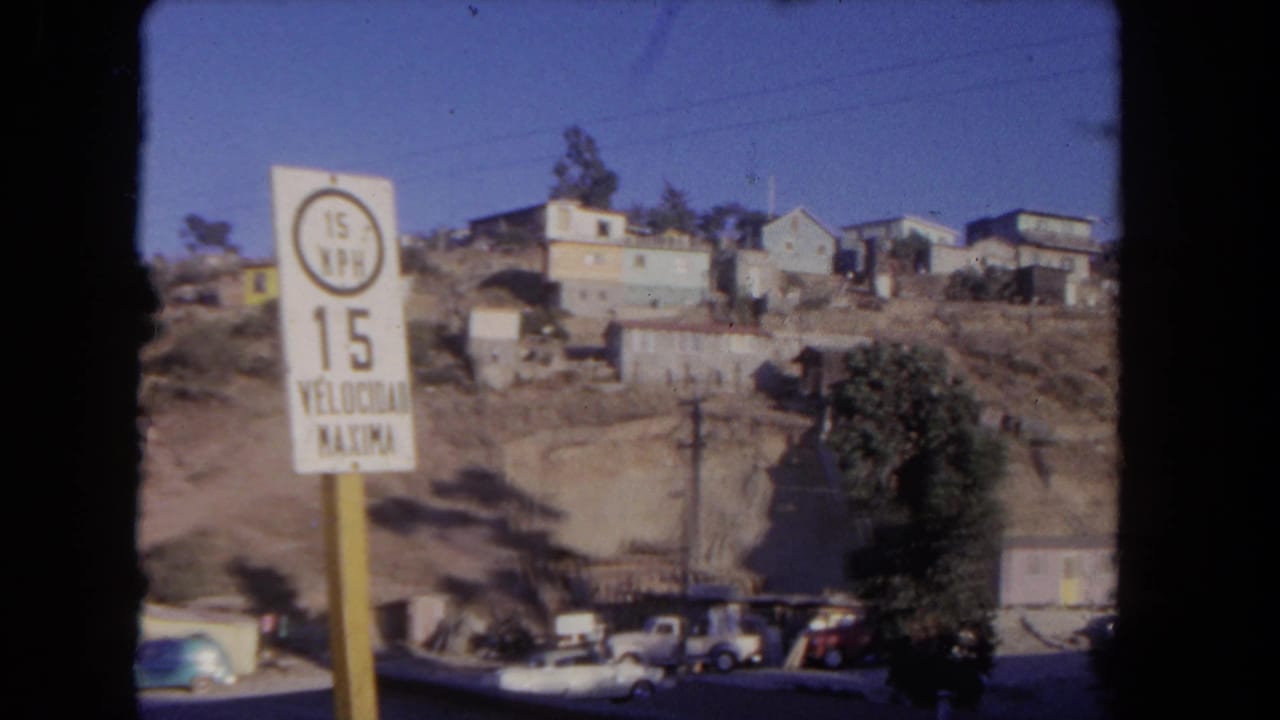 Speed-limit sign and hillside homes above a street with parked cars.