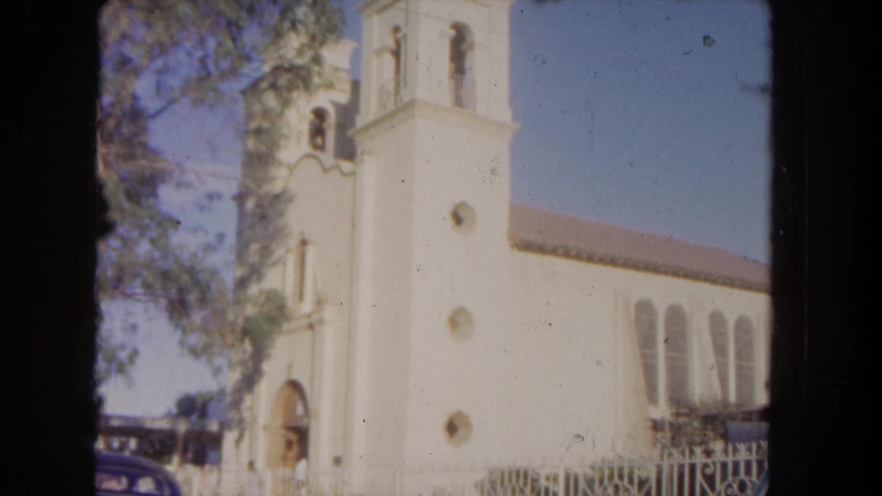 Tall white church tower and side windows seen beside trees and a parked car.
