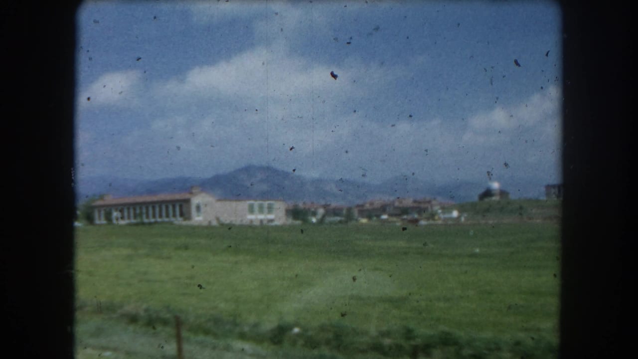 8mm color home-movie frame circa 1962 continuing the driving-past view of a meadow and building near Summit County, Colorado, with mountain backdrop.