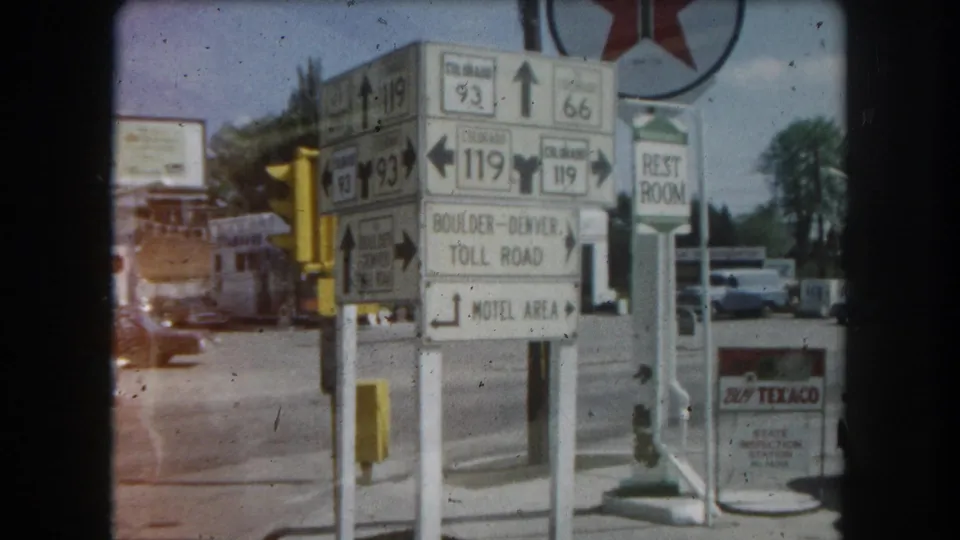 8mm home-movie frame circa 1962 at a Colorado highway junction: route signs for Colorado 93, 66, and 119, Boulder-Denver Toll Road, Motel Area, Rest Room, and a Texaco service station logo.