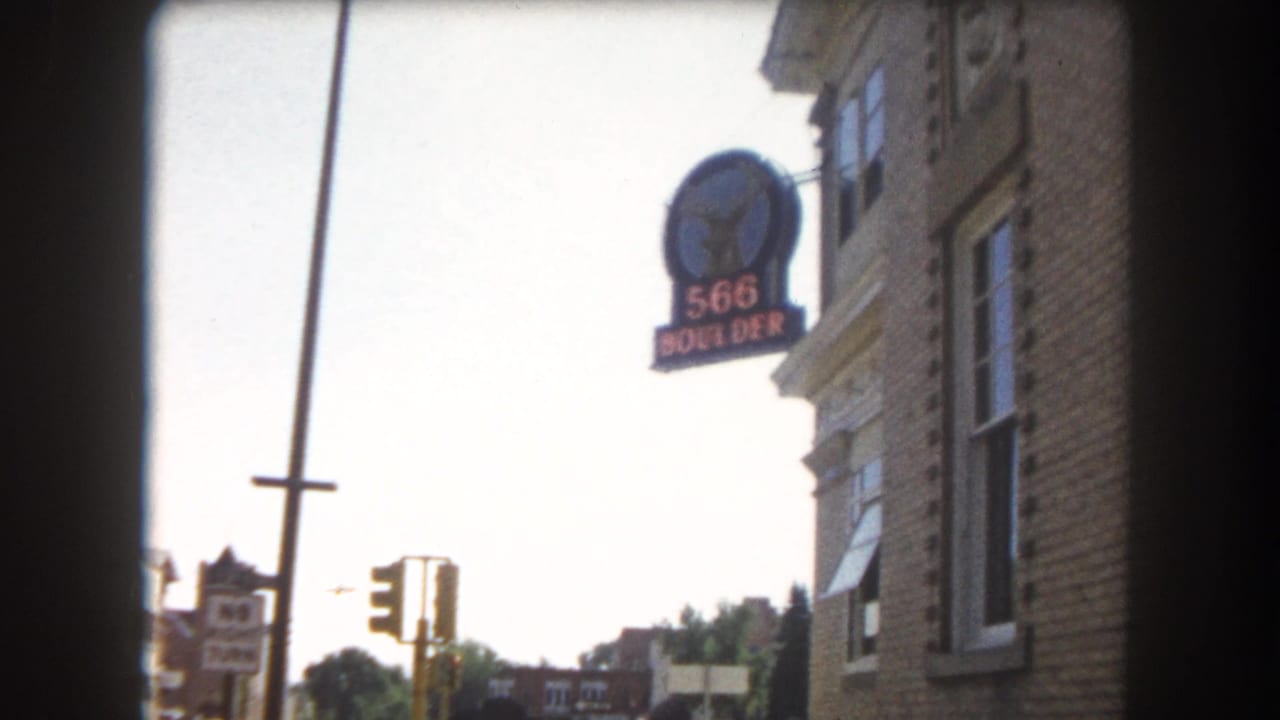 Brick corner building with a '566 BOULDER' hanging sign and traffic light; dark 8mm vignette borders frame the shot.
