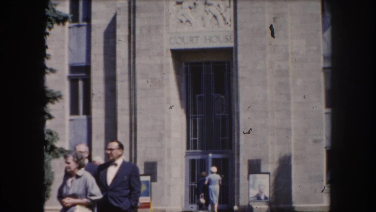 Couple posed near the courthouse entrance in Summit County, Colorado, circa 1962, with pedestrians visible in the background.