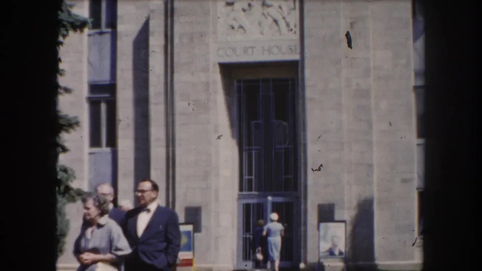 Couple posed near the courthouse entrance in Summit County, Colorado, circa 1962, with pedestrians visible in the background.