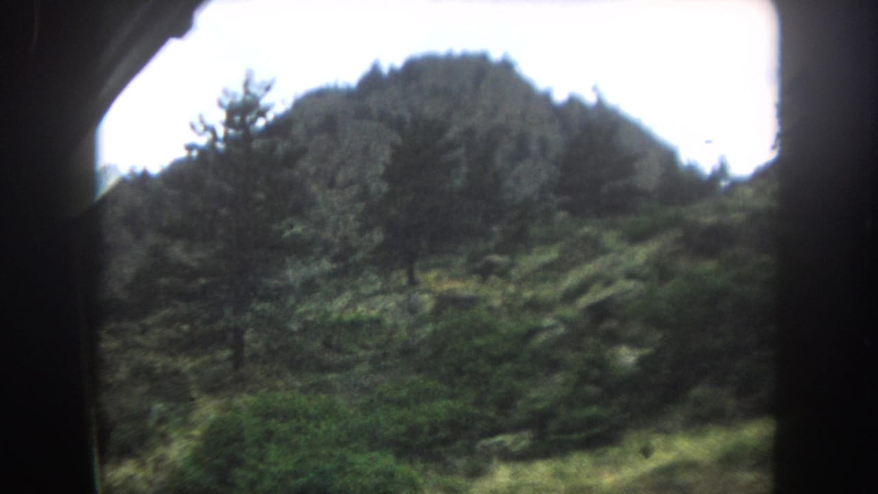 Rocky mountain peak with forested slopes seen through a train window on 8mm film.
