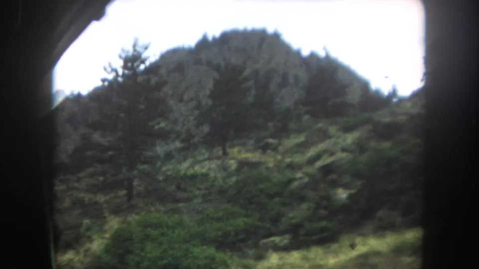8mm color film of a rocky mountain summit with coniferous tree cover on its slopes, likely Summit County, Colorado, circa 1962.