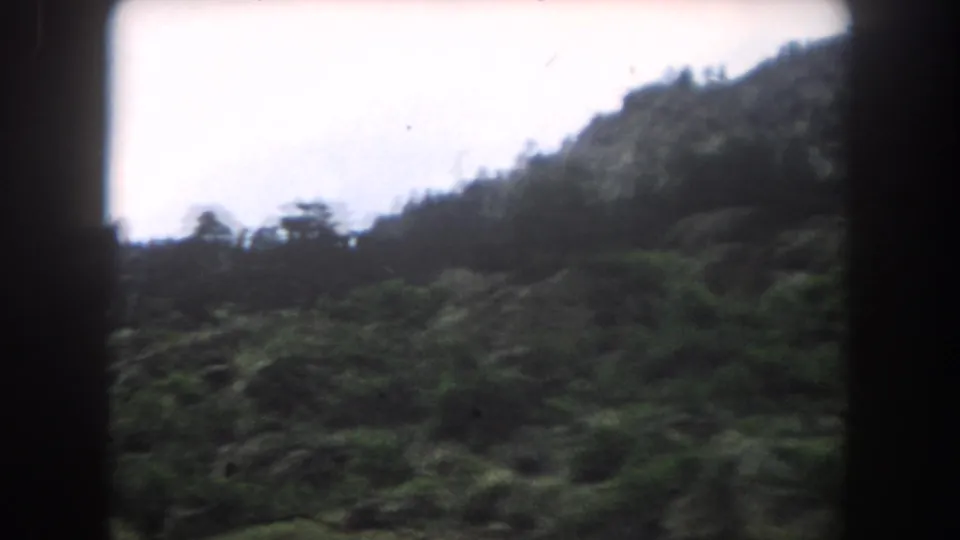 8mm color film showing a dark rocky ridge with pine tree silhouettes against a pale overcast sky, consistent with Colorado mountain terrain, circa 1962.