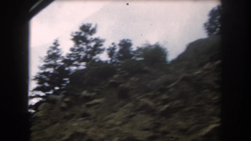 8mm home movie frame circa 1962, motion-blurred conifers and scrubby hillside viewed from a moving car, possibly Summit County, Colorado