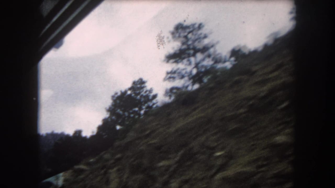 8mm home movie view through a train window of a steep Rocky Mountain slope dense with evergreen trees, circa 1962, Summit County, Colorado.