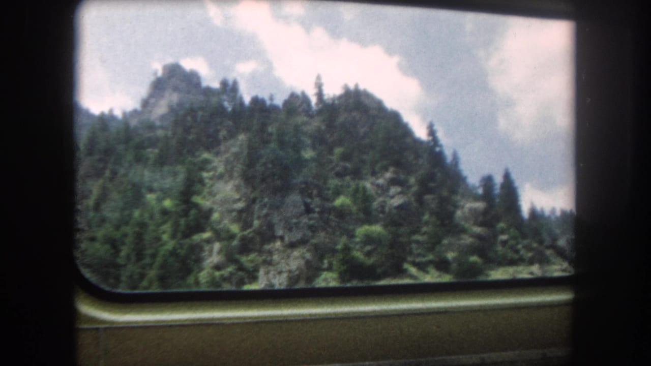 8mm home movie looking through a rounded train window at a rocky peak above dense conifers, Summit County, Colorado, circa 1962.