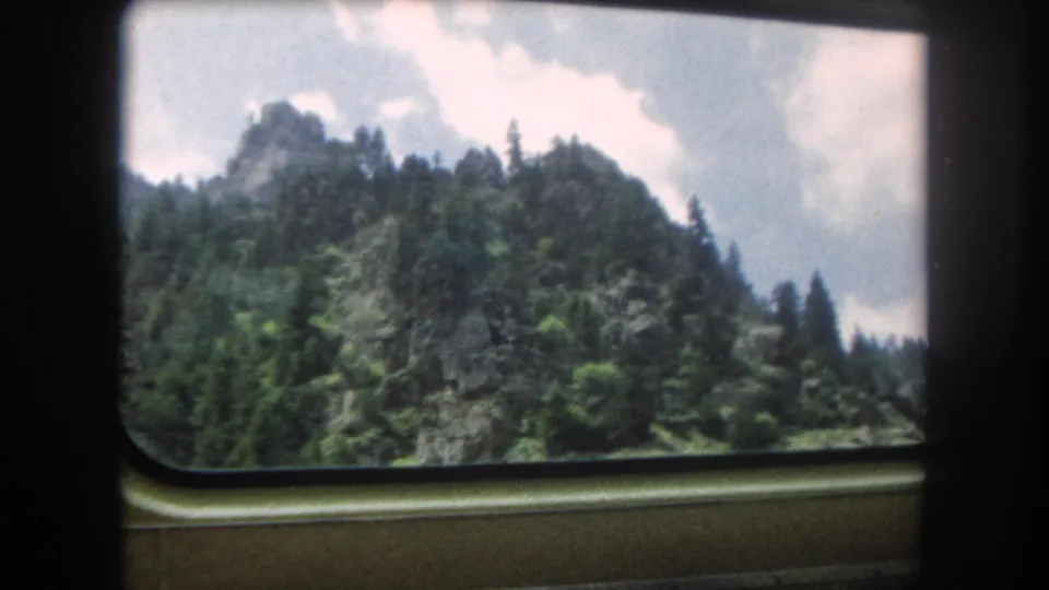 8mm home movie looking through a rounded train window at a rocky peak above dense conifers, Summit County, Colorado, circa 1962.