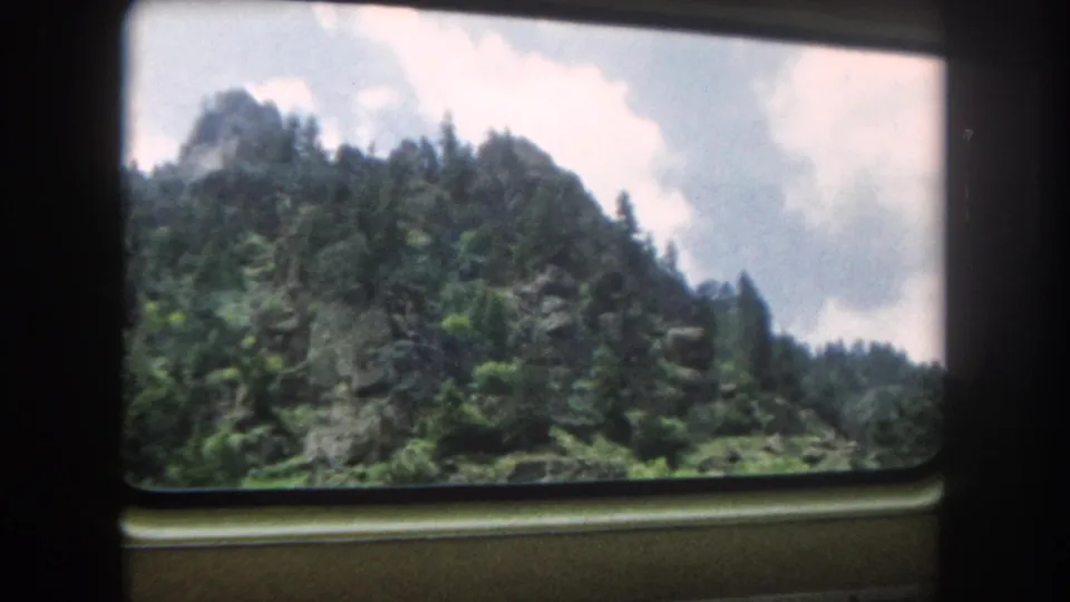 8mm travel footage through a train window showing a rocky Colorado mountain summit and dense evergreen forest under a partly cloudy summer sky, circa 1962.