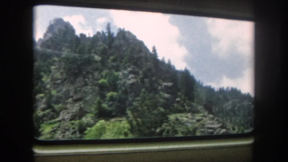 8mm home movie from a train window showing a rocky mountain peak above conifers, Summit County, Colorado, circa 1962, as the train continues its journey.