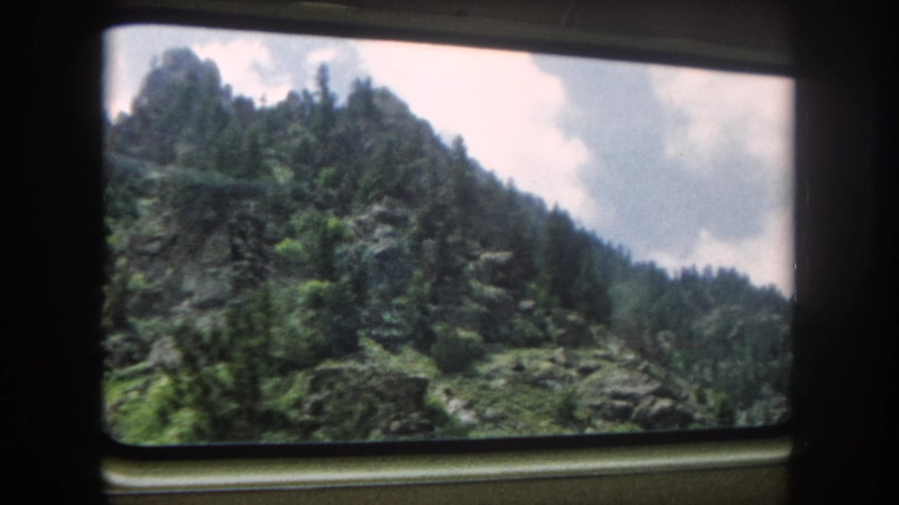 Train window view of conifer-covered Rocky Mountain slopes, likely Summit County, Colorado, circa 1962, shot on 8mm film.