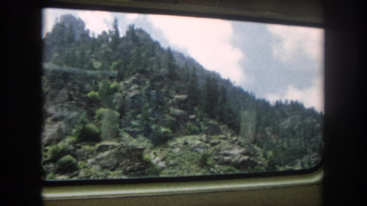 Continued train window view of forested mountain terrain consistent with Colorado Rocky Mountains, circa 1962 8mm footage.
