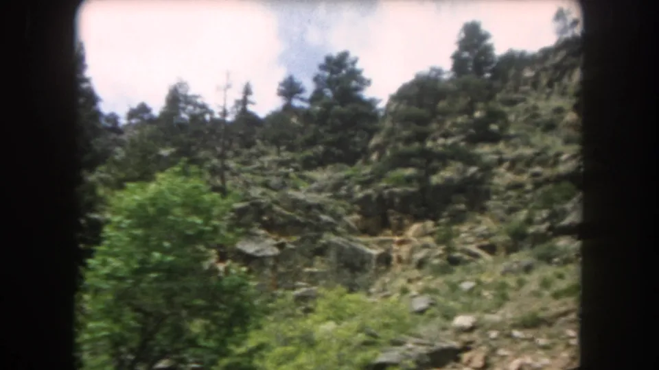 8mm frame circa 1962 showing a steep, boulder-strewn slope covered in evergreen trees in what is described as Summit County, Colorado.