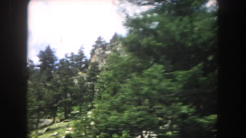 8mm home-movie frame circa 1962 showing a steep rocky canyon wall above a conifer forest, consistent with Summit County, Colorado terrain.