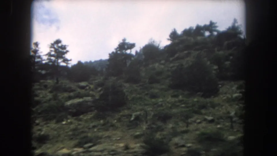 Rugged mountain slope with scattered conifers and boulder outcroppings, Summit County Colorado, 1962, shot from a moving vehicle on 8mm.
