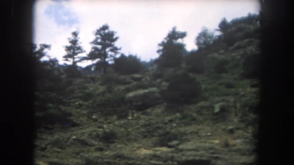 Open rocky hillside with pine silhouettes against a partly cloudy sky, Summit County Colorado, 1962 8mm home movie.