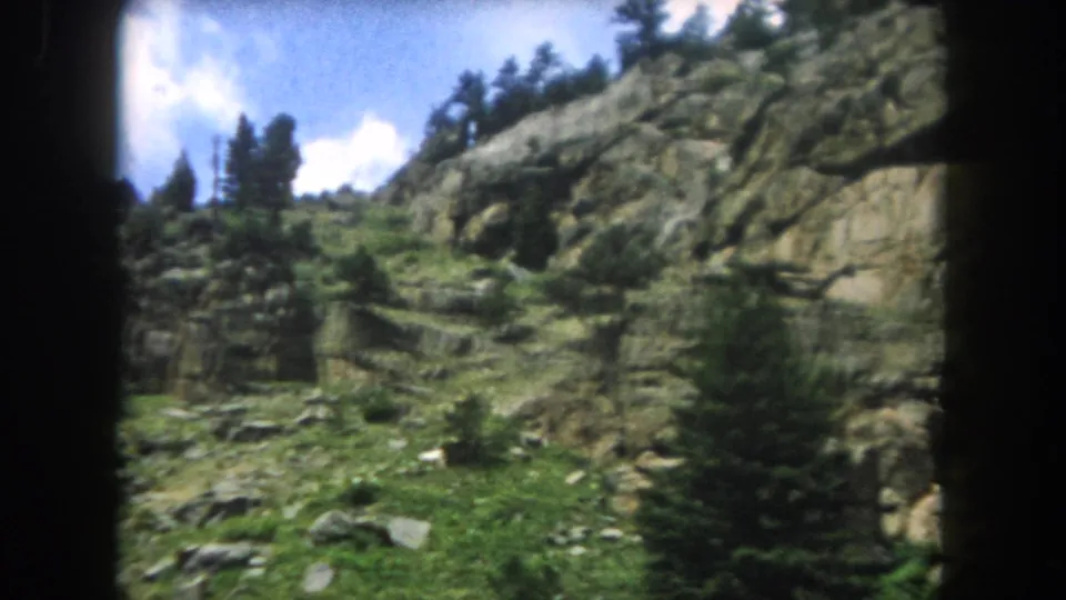 Granite boulder face with sparse alpine vegetation and blue sky with cumulus clouds, Summit County Colorado, 1962 8mm home movie.