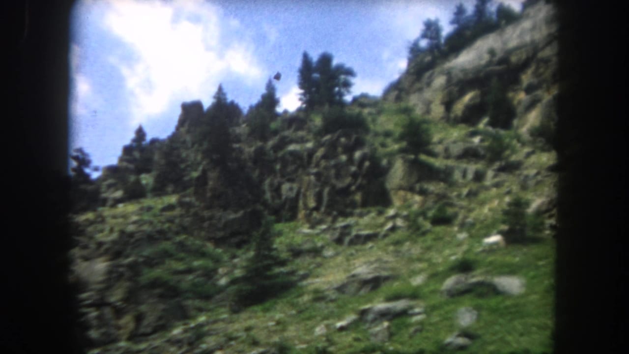 8mm home movie frame from 1962 showing a rocky ridge and silhouetted evergreen trees against blue sky, Summit County, Colorado.