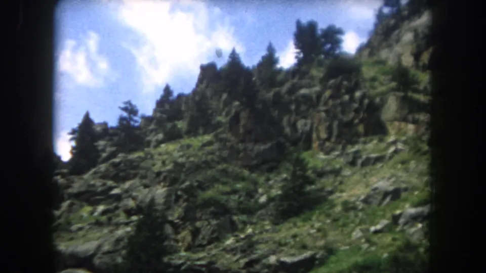 8mm film frame from 1962 showing a rocky mountain ridgeline with conifers and vivid blue sky, Summit County, Colorado.
