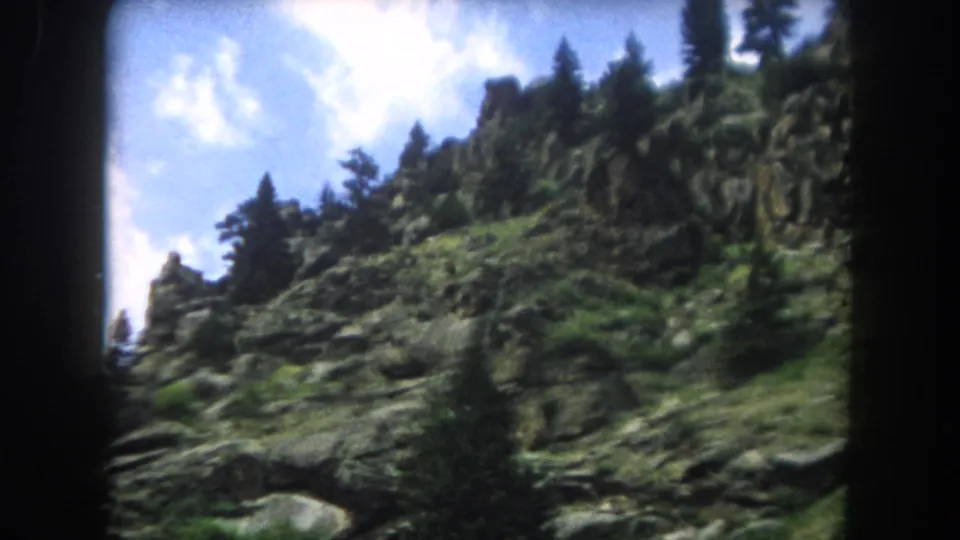 8mm home movie frame from 1962 showing craggy rock outcrops and conifers on a Colorado mountain slope, Summit County.
