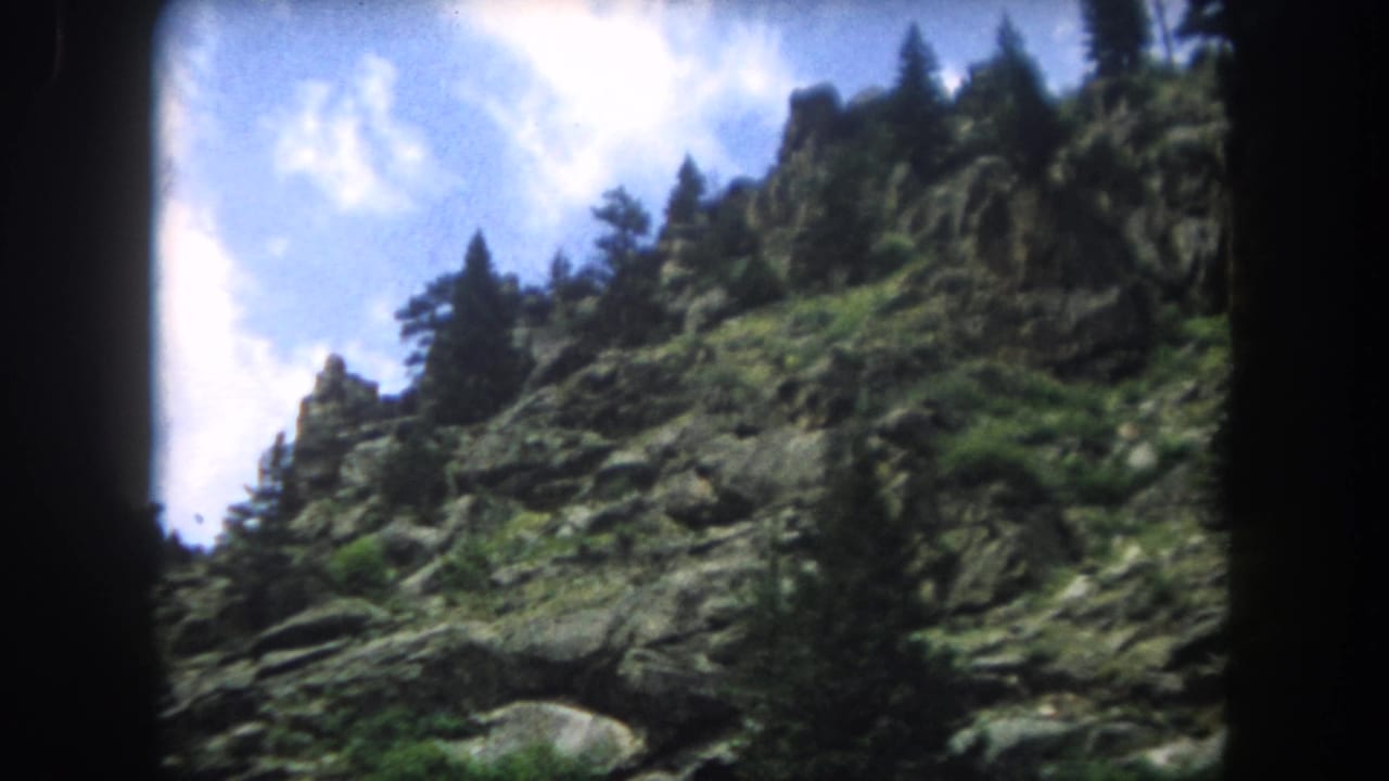 8mm home movie frame of a rugged Rocky Mountain slope with conifers and blue sky, likely Summit County Colorado, 1962