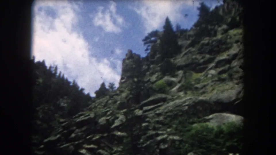 8mm frame of a forested granite mountain face with prominent rock outcroppings, consistent with 1962 Colorado Rocky Mountains