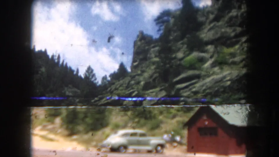 Final 8mm frame transitioning to a parked light green classic sedan beside a red outbuilding, Summit County Colorado area, 1962