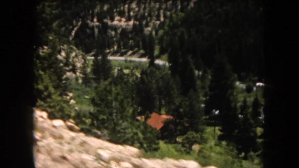 A sweeping high-angle view of a forested valley with a winding road and a red-roofed building below, consistent with Summit County, Colorado, circa 1962.