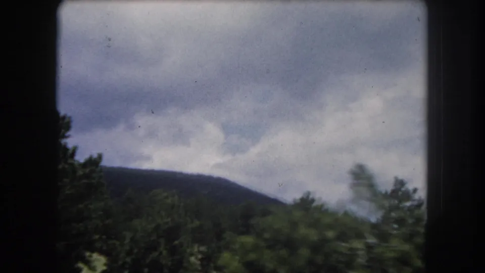 8mm color shot of a mountain ridge and overcast cloud sky with conifer treeline in the foreground, consistent with Colorado Rocky Mountain scenery circa 1962.