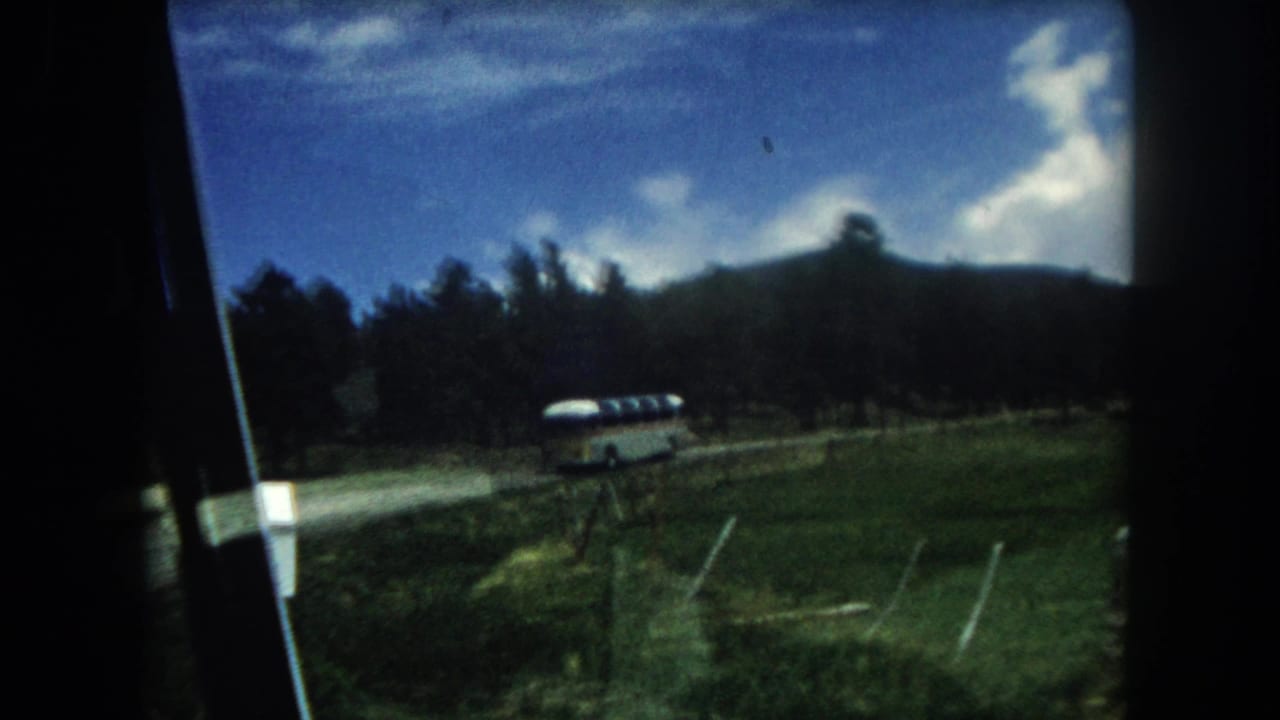1960s 8mm home movie point-of-view through a car window: a mid-century coach bus travels a rural road through a Summit County, Colorado mountain valley, c. 1962.