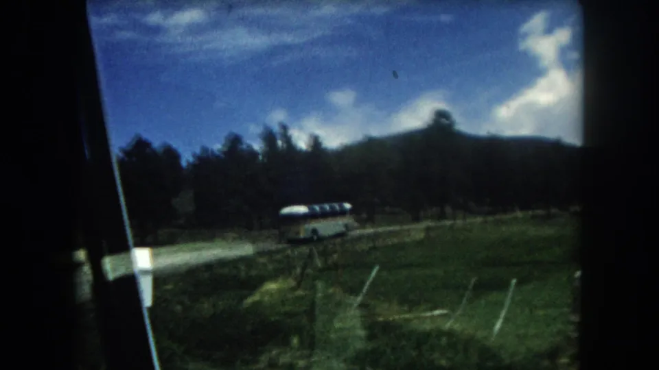 1960s 8mm home movie point-of-view through a car window: a mid-century coach bus travels a rural road through a Summit County, Colorado mountain valley, c. 1962.
